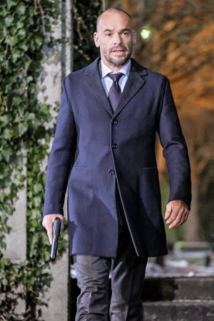 Paul Blackthorne Wearing A Navy Blue Color Styish Wool Coat In Dama Series Arrow he holding a gun in right hand