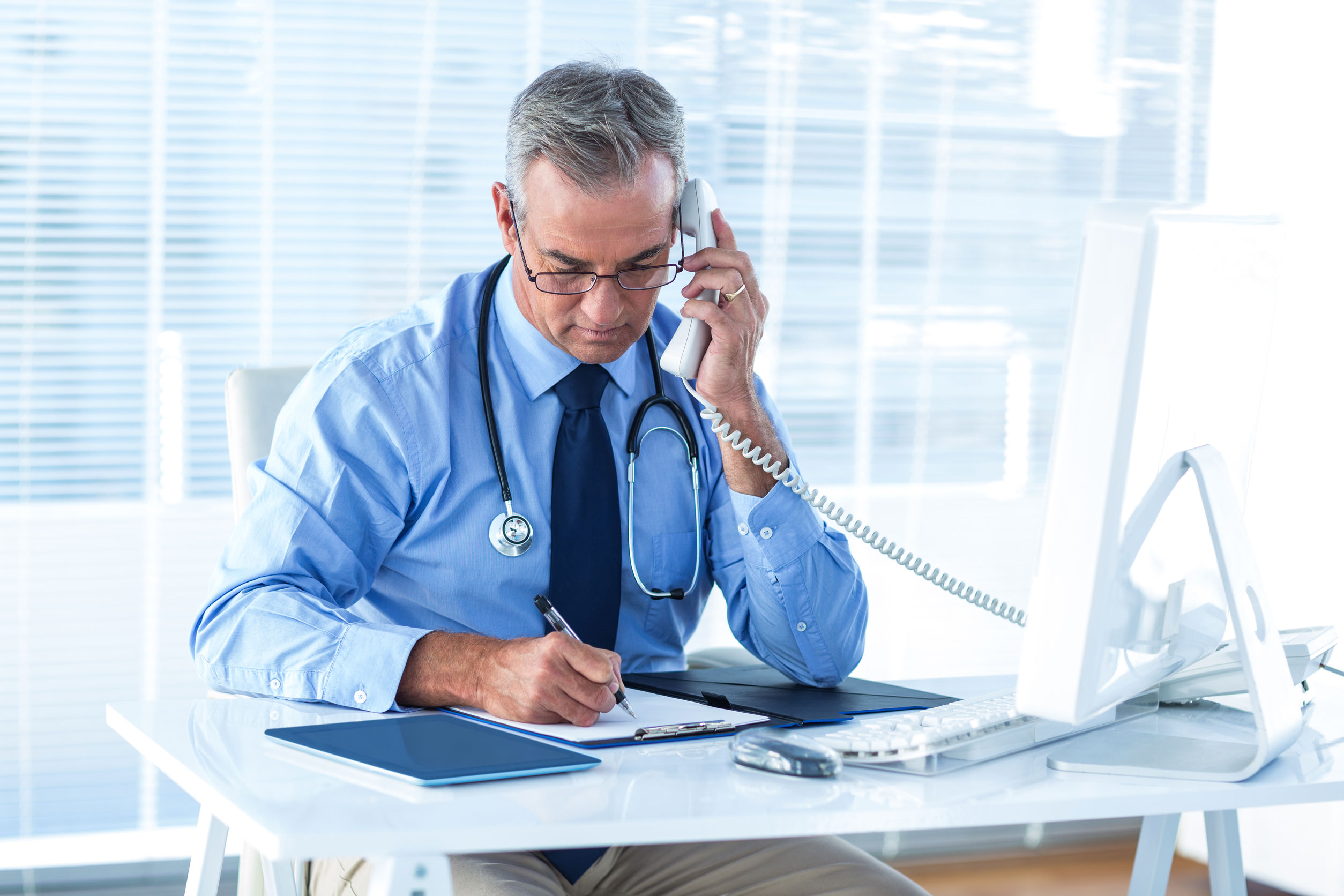 Male doctor writing document white talking on telephone in hospital